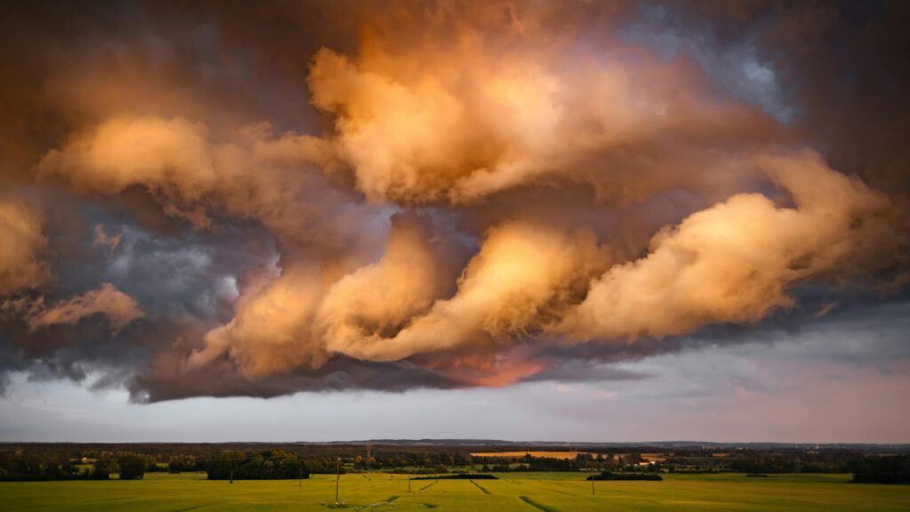 Epic storm clouds illuminated by the sunset over expansive green fields, showcasing a dramatic weather phenomenon.